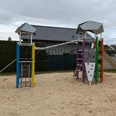 Spielplatz Varusweg Moderner Spielplatz mit Klettergerüst, Rutsche und Sandfläche, umgeben von Häusern und Hecken.