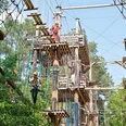Rietberg_schnurstracks Kletterpark.jpg Mehrere Menschen klettern in einem Hochseilgarten zwischen Bäumen unter klarem Himmel.