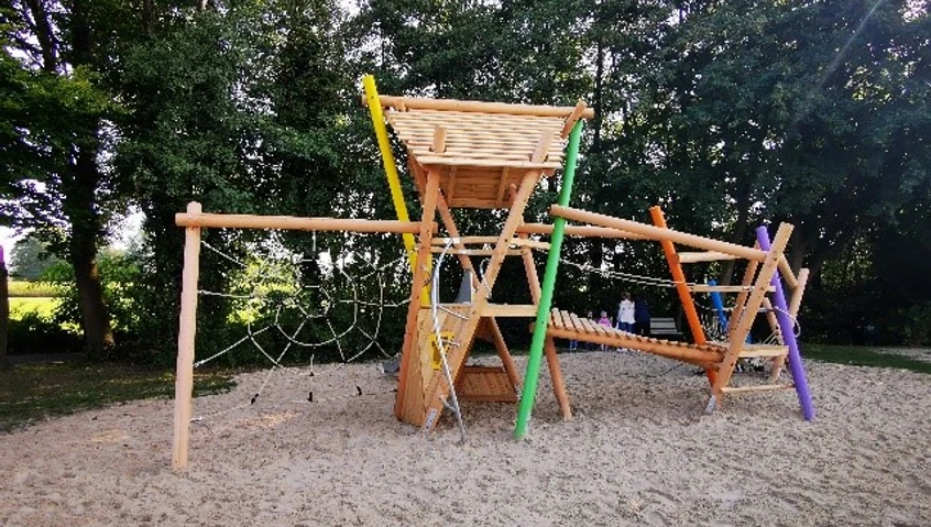 Kombispielgerät Ein moderner Spielplatz aus Holz, umgeben von Bäumen, bietet Kletter- und Balanciermöglichkeiten.