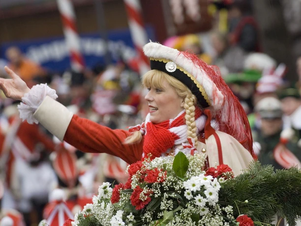 Funkemariechen Rote Funken Eine junge Frau in traditionellem rot-weißen Kostüm lächelt und hat Blumen schmückend in der Hand.
