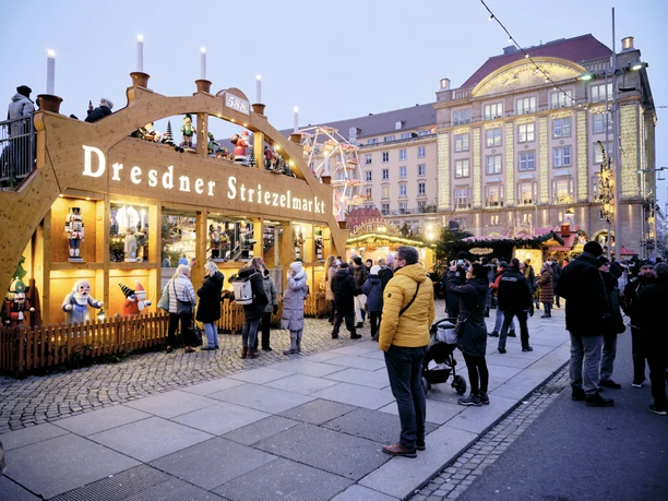 People visit the Dresden Striezelmarkt with its illuminated decorations and wooden market stalls.