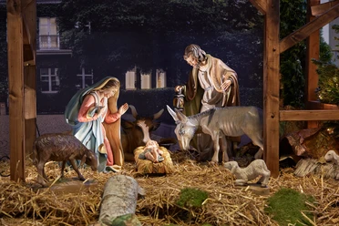 Weihnachtskrippe Krippenszene mit Figuren von Maria, Josef, Jesuskind, einem Esel und Ochse auf Stroh unter einem Holzstall.