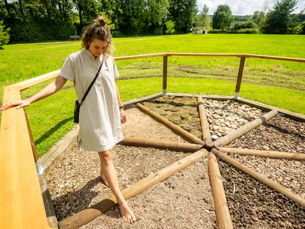 Barfusspfad Kurpark Bad Holzhausen Barfußpfad mit Holzgeländer im Kurpark Bad Holzhausen, Besucher genießt verschiedene Bodenbeläge.