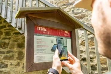 Ein Besucher scannt mit dem Handy einen QR-Code an einem Infobrett vor der Burg Limberg.