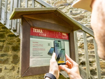 Ein Besucher scannt mit dem Handy einen QR-Code an einem Infobrett vor der Burg Limberg.