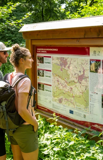 Zwei Wanderer lesen aufmerksam eine Informationstafel zu Wanderwegen im Wiehengebirge.