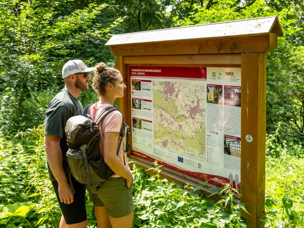 Zwei Wanderer lesen aufmerksam eine Informationstafel zu Wanderwegen im Wiehengebirge.