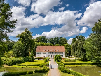 Historisches Gebäude im Kurpark Bad Holzhausen, umgeben von gepflegtem Garten mit Teich und Bäumen.