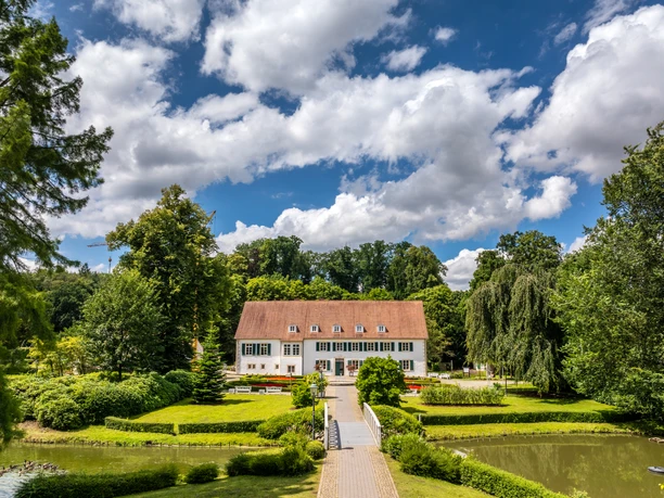 Historisches Gebäude im Kurpark Bad Holzhausen, umgeben von gepflegtem Garten mit Teich und Bäumen.