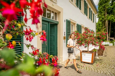 Kurpark Bad Holzhausen Eine lächelnde Frau spaziert entlang eines Gebäudes mit grünen Fensterläden und Blumen.