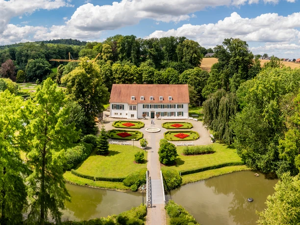 Luftaufnahme des Kurparks Bad Holzhausen mit symmetrischen Blumenbeeten und einem historischen Gebäude.