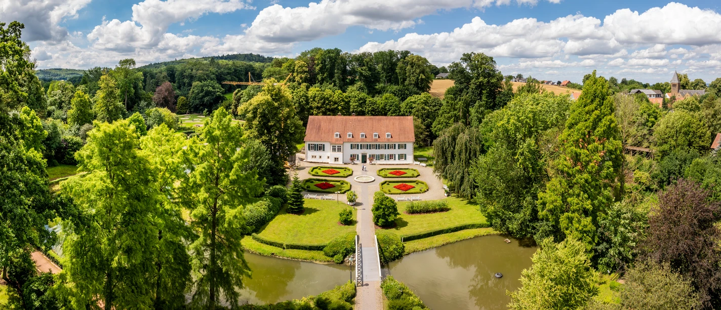 Luftaufnahme des Kurparks Bad Holzhausen mit symmetrischen Blumenbeeten und einem historischen Gebäude.