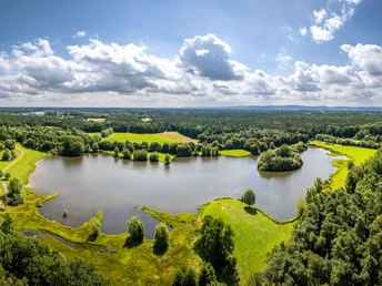 Wunderschöner See mit bewaldeten Ufern, umgeben von grünen Wiesen und sanften Hügeln.