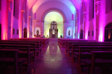 LichterHimmel-Kirche Westerwiehe (1).JPG Kirchenschiff beleuchtet in violettem und blauem Licht, mit Holzbänken und einem Altar im Hintergrund.