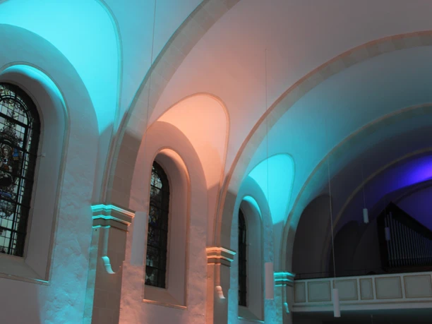 LichterHimmel-Kirche Westerwiehe (3).jpg Bunte Beleuchtung akzentuiert die imposanten Bögen und Fenster einer historischen Kirchenarchitektur.