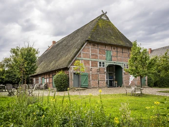 Touristinfo und Biosphärenzentrum Amt Neuhaus Touristinfo und Biosphärenzentrum Amt NeuhausTourist information and biosphere center Amt NeuhausOffice du tourisme et centre de biosphère Amt NeuhausToeristische informatie en biosfeercentrum Amt NeuhausTuristinformation og biosfærecenter Amt NeuhausGammal tegelbyggnad med halmtak och gröna portar omgiven av trädgård och utemöbler.