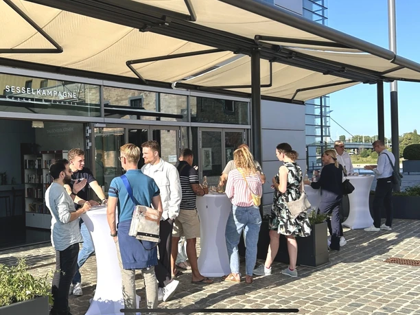 Hafenterrasse mit Sonnenmarkise People meet in the sunshine on the terrace with white bar tables and awning