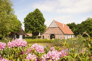 Landluftkonzert_Fotocredit-NWD.jpg Fachwerkhäuser mit rotem Giebel, umgeben von blühenden Rhododendren und einem kleinen Teich.
