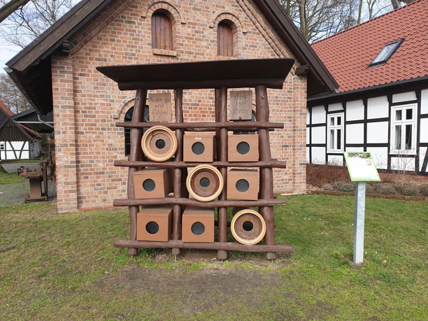 Ein kunstvolles Insektenhotel aus Holz und Ziegeln vor einem traditionellen Backsteingebäude.