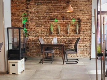 Innenraum mit Backsteinwand, modernen Hängelampen und zwei dunkelbraunen Stühlen an einem Tisch.