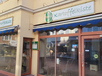 Außenansicht des Restaurants "Kartoffelkiste" mit gläserner Fassade und grün-weißer Beschilderung.