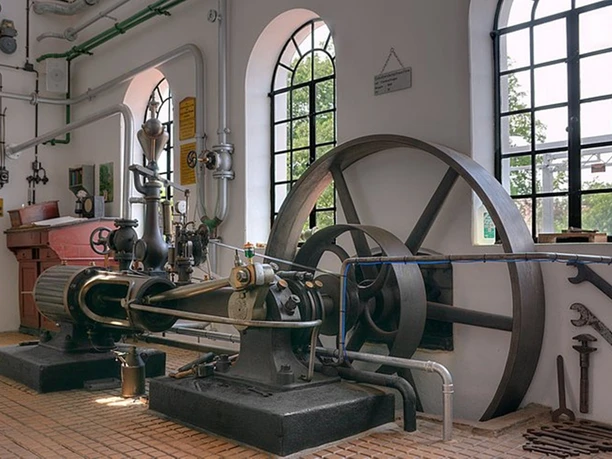 Alte Brennerei Dampfmaschine Dampfmaschine mit sichtbaren Kolben und Schwungrad im historischen Industriemuseum, helle Wände.