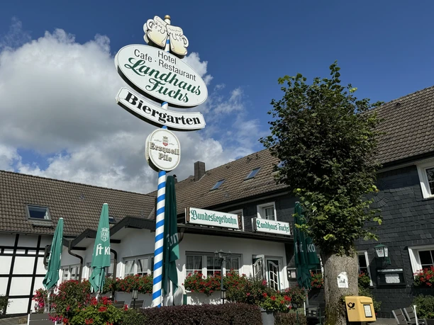 Landhaus Fuchs - Außenansicht Hotel Landhaus Fuchs in Kürten mit Biergarten, umgeben von Pflanzen, mit Sonnenschirmen.