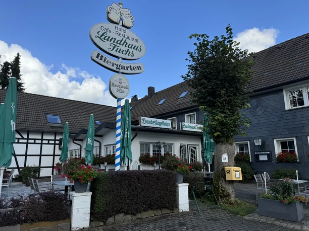 Landhaus Fuchs - Außenansicht Vor einem Fachwerkhaus stehen sonnenschirmbedeckte Tische des Landhaus Fuchs, ein gemütliches Hotel.