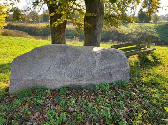 Findling Großer Findling auf einer Wiese nahe zwei Bäumen, flankiert von einer einfachen Holzbank im Herbst.
