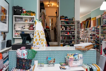 Toddlin Town Kinderbekleidung – Shopping in Leipzig In dem Kinderbekleidungsgeschäft Toddlin Town stapeln sich viele bunte Stoffmuster – Handarbeit, Kreativität, Kindermode