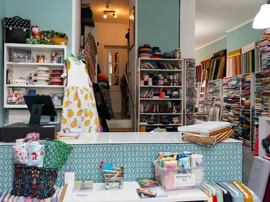 Toddlin Town Kinderbekleidung – Shopping in Leipzig In dem Kinderbekleidungsgeschäft Toddlin Town stapeln sich viele bunte Stoffmuster – Handarbeit, Kreativität, Kindermode