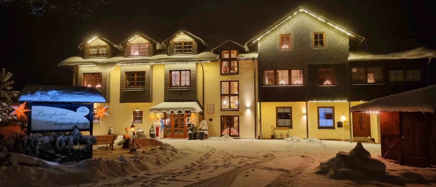 Winternachtopname van een verlicht hotel met besneeuwde gevel en uitnodigende sfeer.