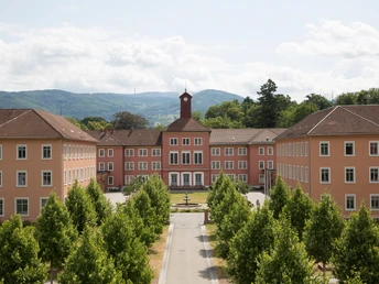 Großes Gebäude mit vielen Fenstern, eine ehemalige Heil-und Pflegeanstalt. Im Hintergrund sieht man die Hornisgrinde.