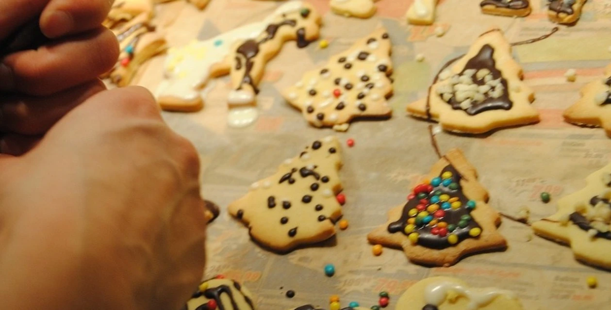 Weihnachtsbacken Hände verzieren bunte Weihnachtskekse mit Schokolade und Streuseln auf einem Backblech.