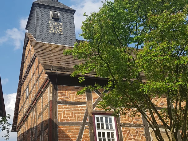 20210514_171704.jpg Fachwerkhauskirche in grüner Umgebung mit Uhrturm und markanter Wetterfahne auf blauem Himmel.