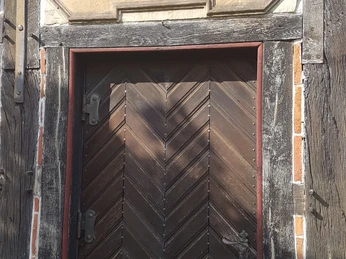 20210514_171309.jpg Eine historische Holztür mit diagonalem Muster und lateinischer Inschrift über dem Eingang.