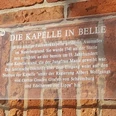 Transparente Plakette an einer Backsteinmauer erklärt die historische Bedeutung der Kapelle in Belle.