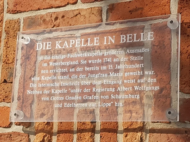 Transparente Plakette an einer Backsteinmauer erklärt die historische Bedeutung der Kapelle in Belle.