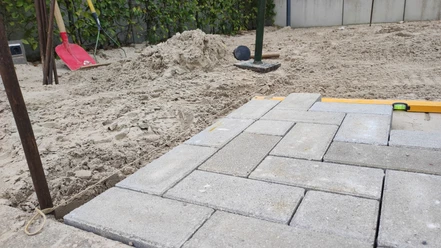 KiWiMedia_Webcode_23562360_Nadja Krause_2024-10-29.jpg Verlegen von Betonpflastersteinen auf Sandbett, Werkzeuge und Wasserwaage liegen daneben.