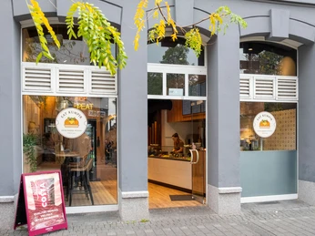 Restaurant Eat Kumpir Graue Hauswand mit Eingang zum Restaurant und Logo auf der Glasfront.Gray house wall with entrance to the restaurant and logo on the glass front.