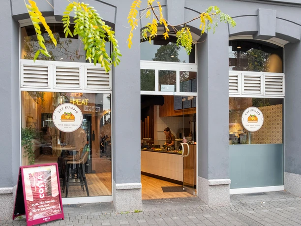 Restaurant Eat Kumpir Gray house wall with entrance to the restaurant and logo on the glass front.