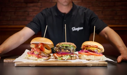 Champions Sports Bar - Gastronomie in Leipzig Ein Koch hält ein Holzbrett, auf dem drei Burger liegen