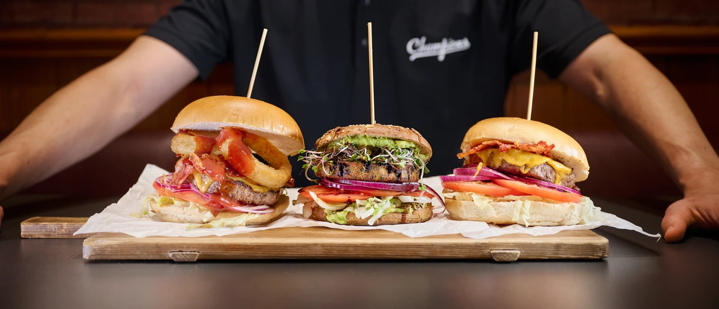 Champions Sports Bar - Gastronomie in Leipzig Ein Koch hält ein Holzbrett, auf dem drei Burger liegen