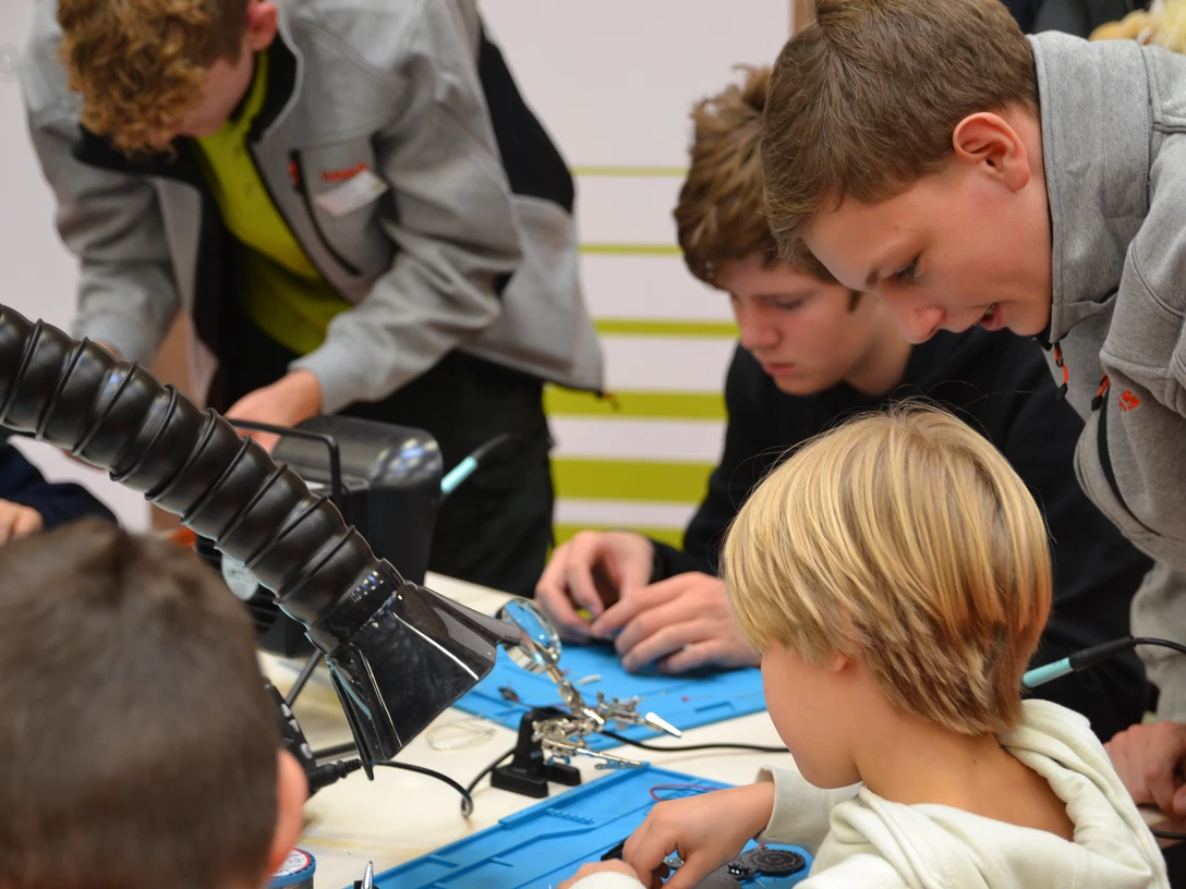 MINT-Mitmach-Tag Kinder und Jugendliche arbeiten konzentriert an technischen Projekten bei einem Workshop am Tisch.
