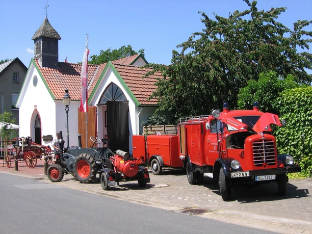 Feuerwehrmuseum Schröttinghausen Rote Feuerwehrfahrzeuge vor einem kleinen Gebäude mit einem Turm und umliegender grüner Vegetation.