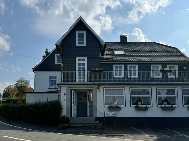 Restaurant Jägerhof - Außenansicht Zweistöckiges Fachwerkhaus mit dunkelblauem Dach und eine weiße Fassade, dekoriert mit Blumenkästen.