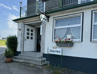 Eingangsbereich eines traditionellen Gasthauses mit Fahne und Blumenkasten am Fenster.
