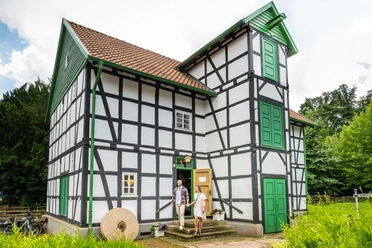 Fachwerkhaus mit grünen Türen, historische Gutwassermühle Hudenbeck, Natur im Hintergrund.
