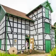 Fachwerkhaus mit grünen Türen, historische Gutwassermühle Hudenbeck, Natur im Hintergrund.