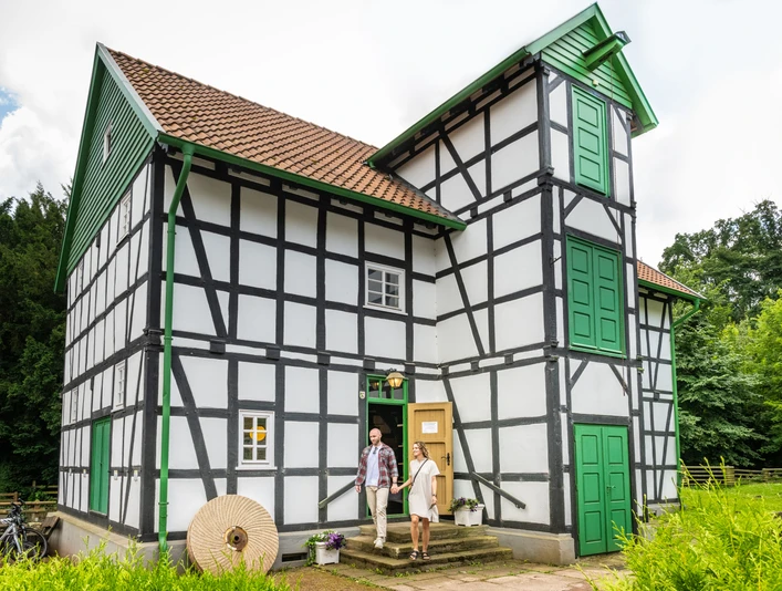 Fachwerkhaus mit grünen Türen, historische Gutwassermühle Hudenbeck, Natur im Hintergrund.